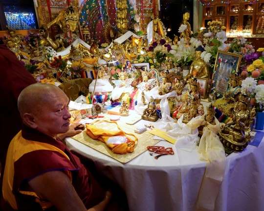 Lama Zopa Rinpoche at night in front of his work table at Kopan Monastery, which has so many statues ... another alter! Nepal, December 2014. Photo by Ven. Roger Kunsang.