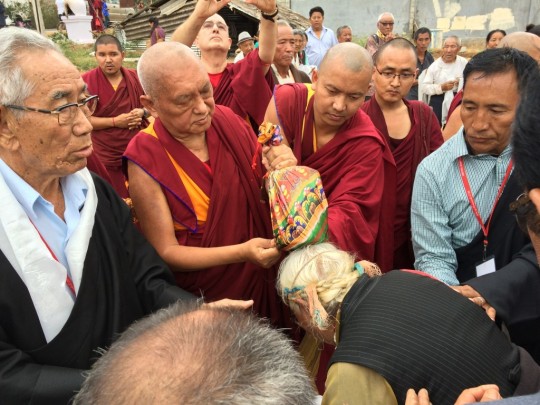 Lama Zopa Rinpoche blessing settlement community members with a prayer wheel containing mantras. 