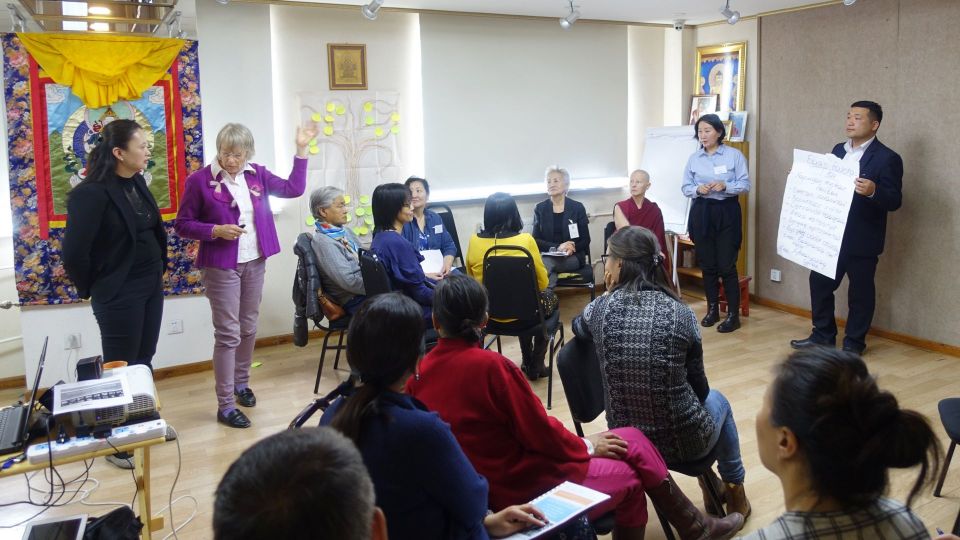 Wendy guiding a group activity where one participant is standing at the front of the room holding a sign and the rest of the group is seated and watching.