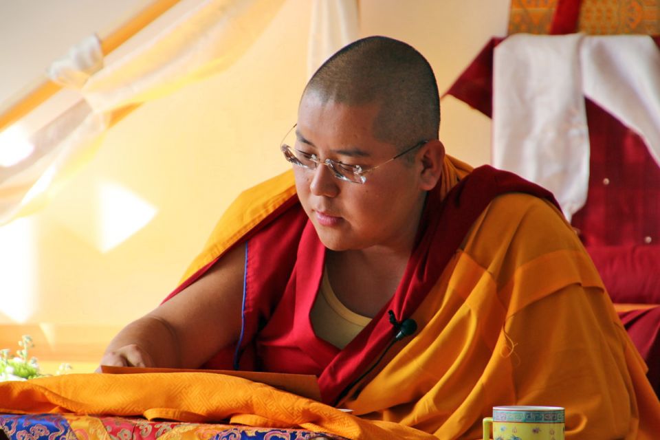 Ling Rinpoche wearing eye glasses and reading Shantideva text resting on a table in front of him while teaching from the throne.
