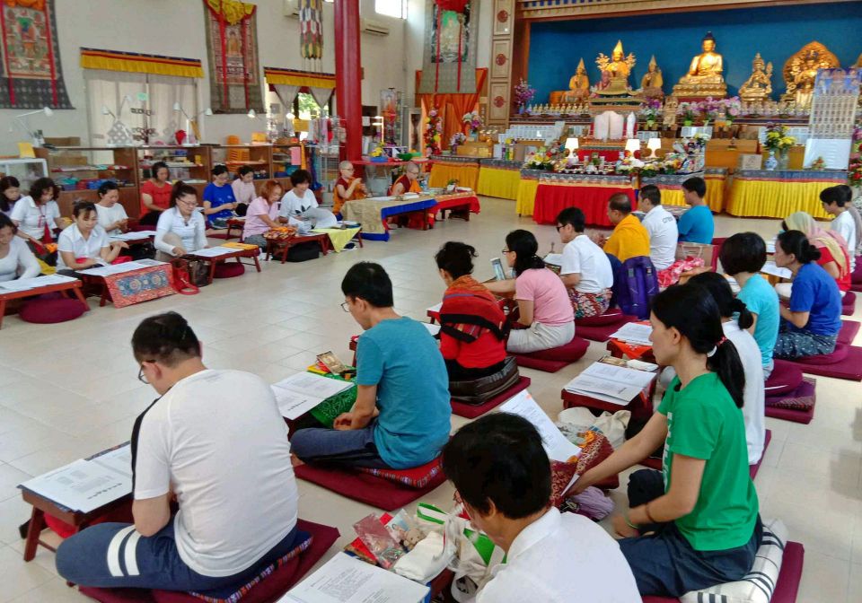 nyung na retreat participants seated on meditation cushions seated in two sections facing each other, with their retreat books open in front of them and engaging in the practice inside of the gompa.