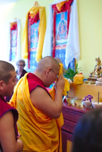 His Eminence Ling Rinpoche making an offering in front of the altar in a sunlight room at shantideva meditation center in brooklyn with colorful tangkas on the yellow walls.