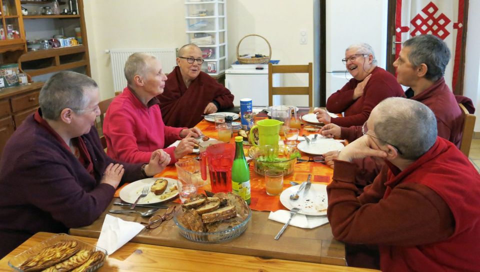 Six western nuns seated together laughing and sharing food in the kitchen at Dorje Pamo Monastery.