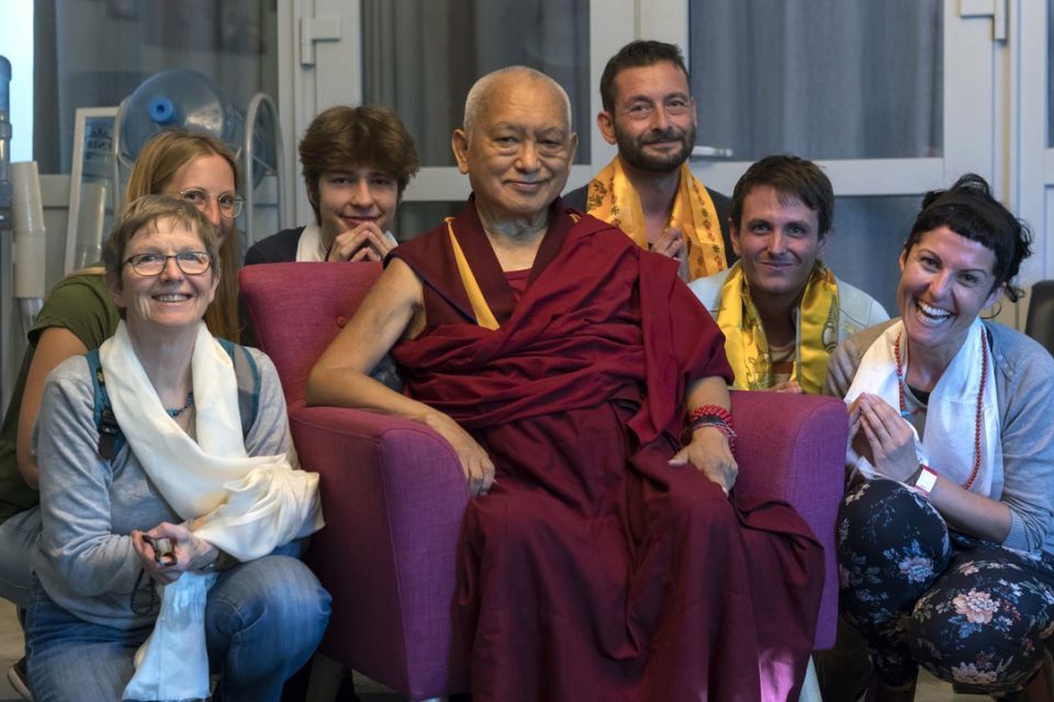 Six students gathered around Lama Zopa Rinpoche who is seated on a purple chair in the middle of the group smiling.