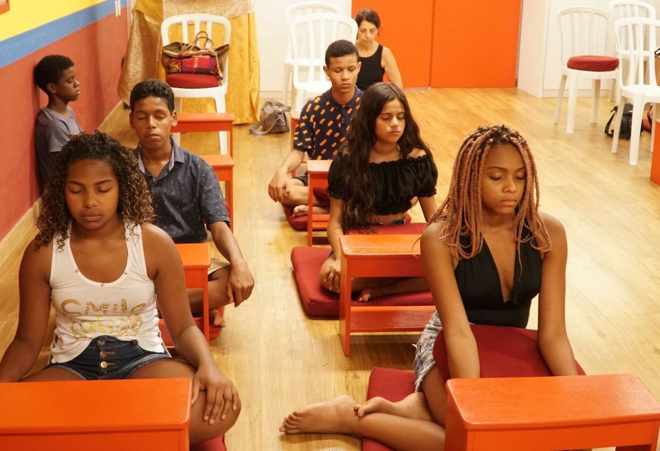 Six teenagers and an adult seated on the floor in the gompa meditating.