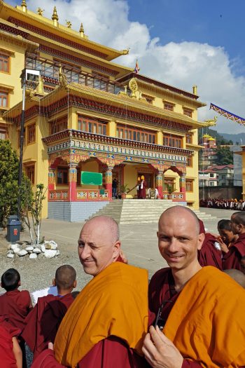 Two monks standing in the sunshine in a courtyard outside of a large Tibetan temple.