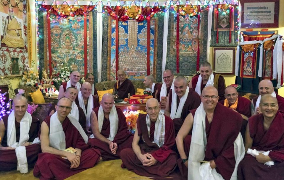 Lama Zopa Rinpoche surrounded by a group of monks wearing white khatas smiling.