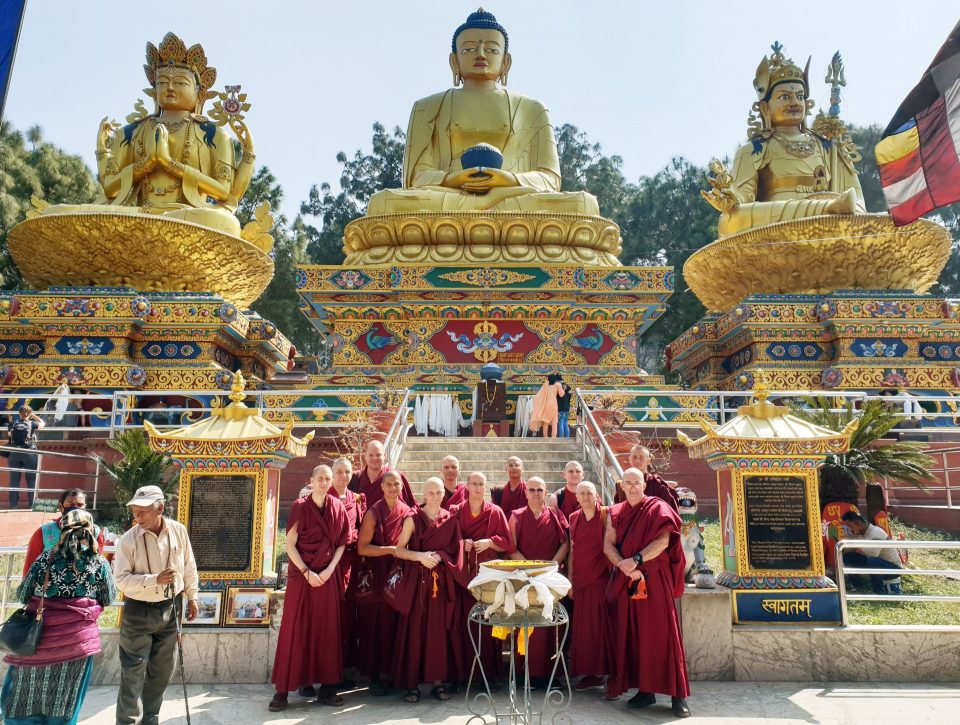 A group of monks standing in front of three huge golden colored statutes.