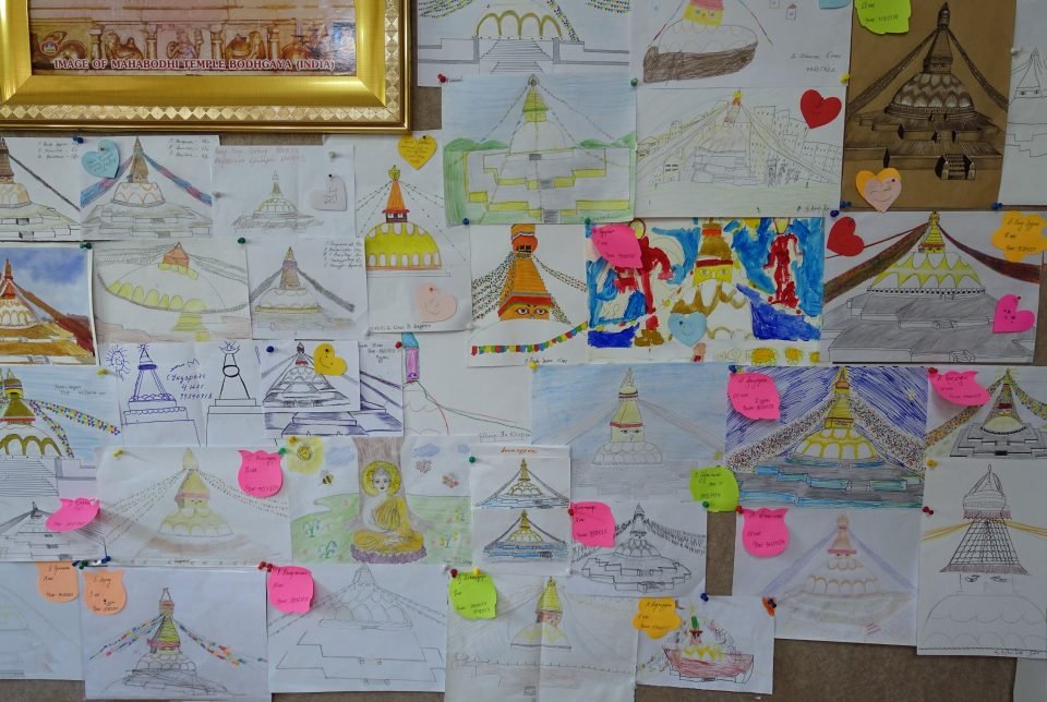 A collection of stupa drawings by different artists pinned to a wall for display.