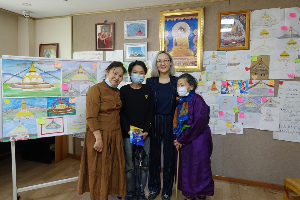 Four people standing together posing for the camera while smiling some wearing face masks.