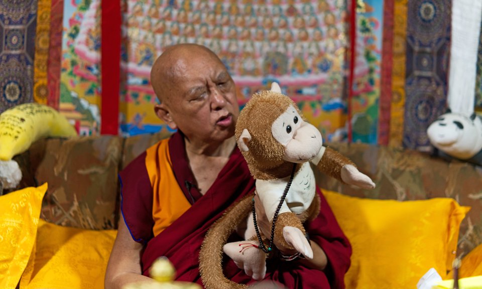 Lama Zopa Rinpoche holding a plush monkey toy, blowing mantras on it