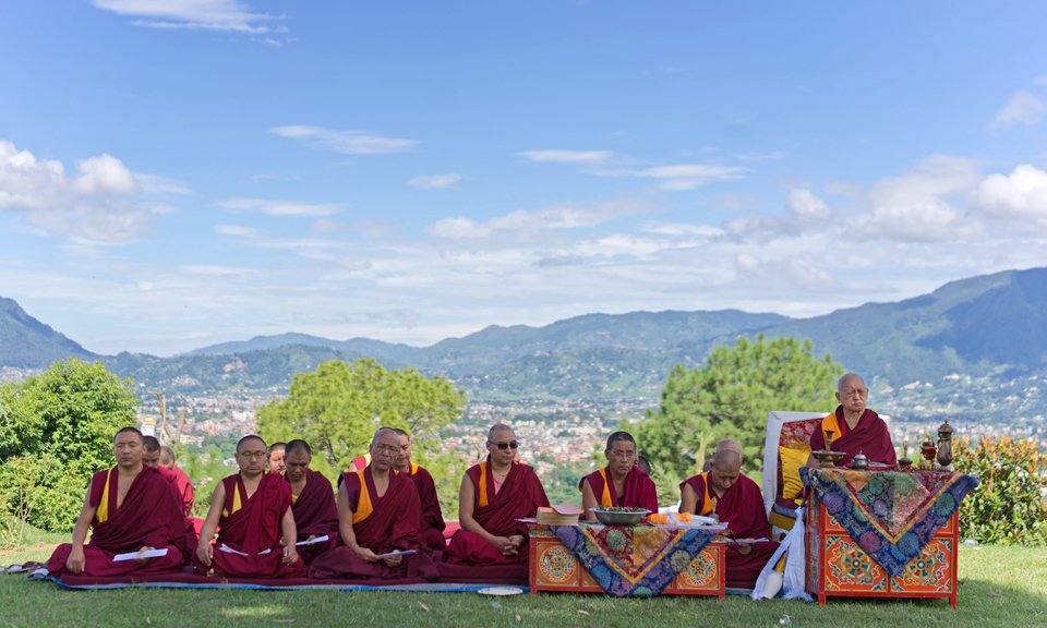 seated monks doing puja outside with view of hills in background