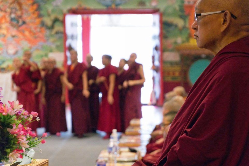 Lama Zopa Rinpoche seated in the gompa with the nuns watching a group debate.