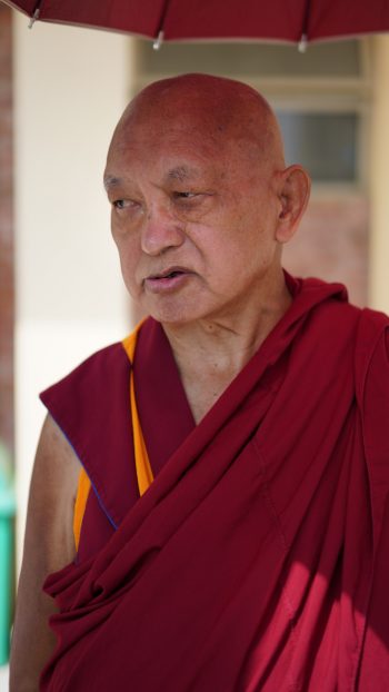 Lama Zopa Rinpoche standing under an umbrella