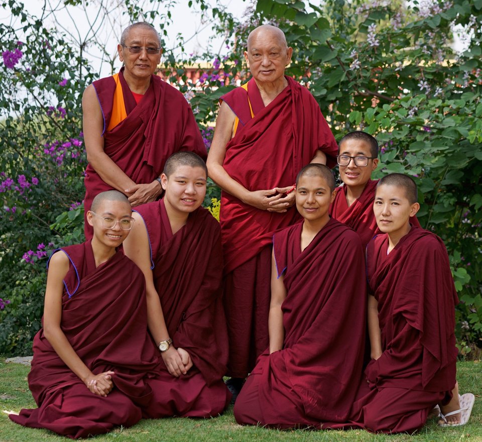 Lama Zopa Rinpoche and Khen Rinpoche Geshe Chonyi standing behind five kneeling nuns in a garden