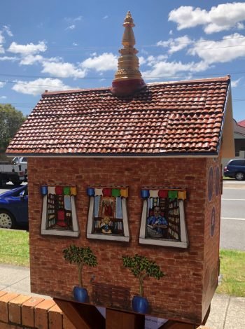 The backside of a small colorful painted box with a roof and stupa spire.