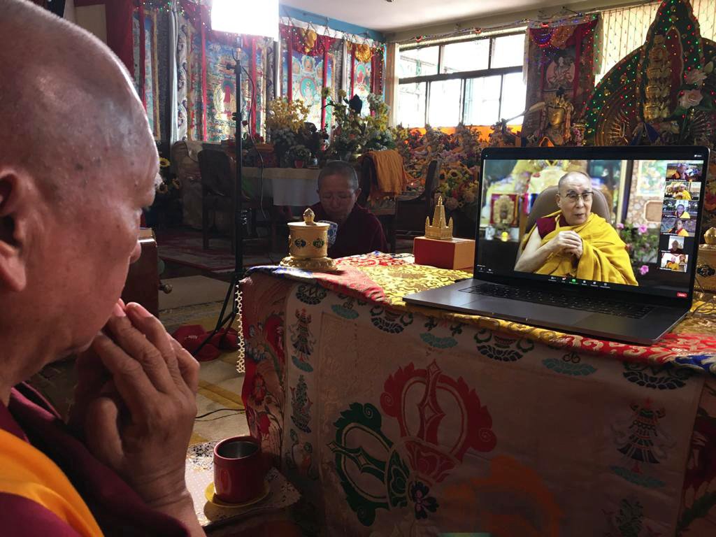 Lama Zopa Rinpoche, with hands in prostration mudra, watching His Holiness the Dalai Lama on a laptop screen