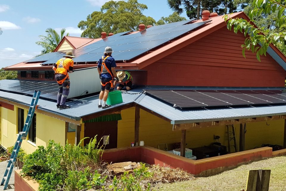 Small construction crew standing on the roof laying solar panels.