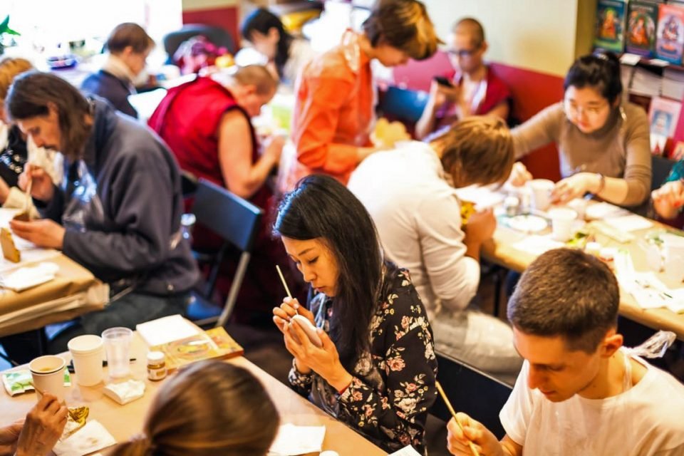 A large group of people seated closely around folding tables and intently painting tsa-tsas.