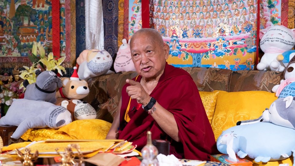 Rinpoche sitting on a couch and gestering with his hand during a teaching