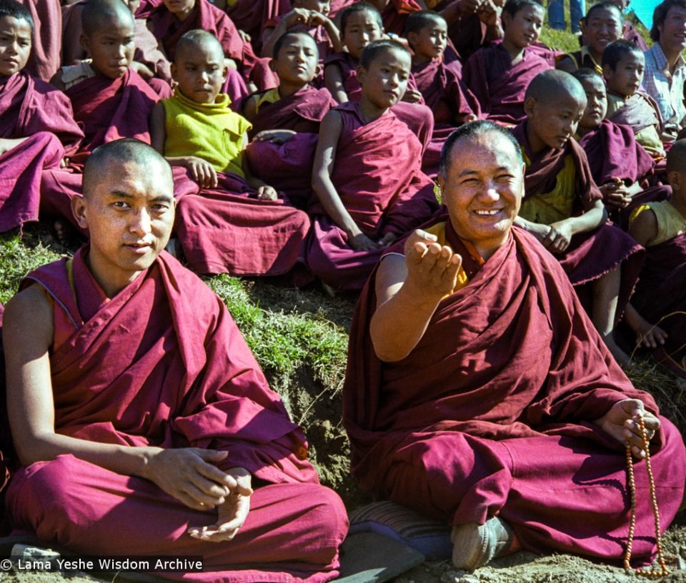 Lama Zopa Rinpoche and Lama Yeshe sitting on Kopan hill with young monks behind them