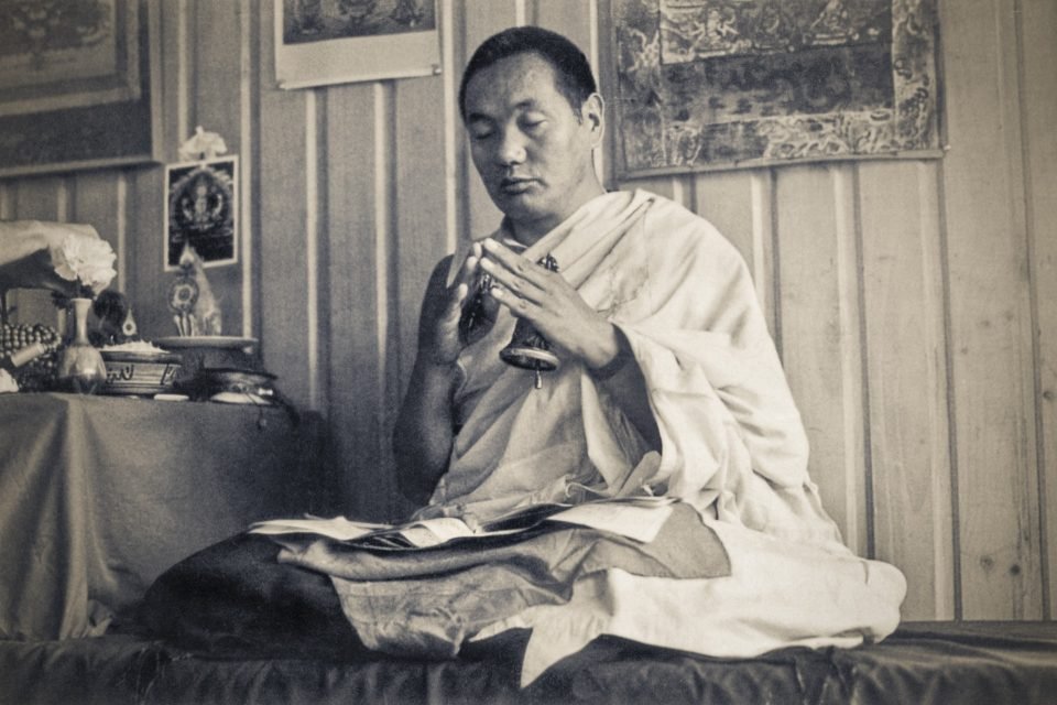 Lama Yeshe holding a dorje and bell with eyes closed on a throne