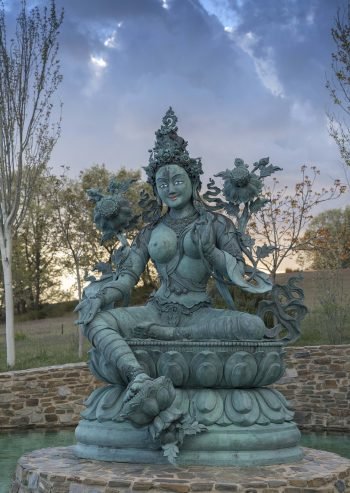 Green Tara statue situated in a small pond on a pedestal under a beautiful spring sky