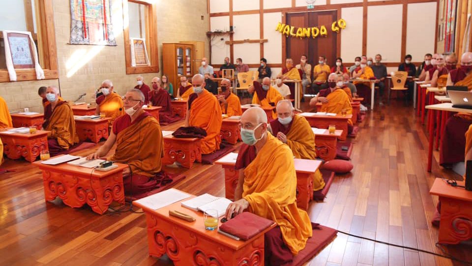 an alter room full of monks sitting at puja tables and wearing masks