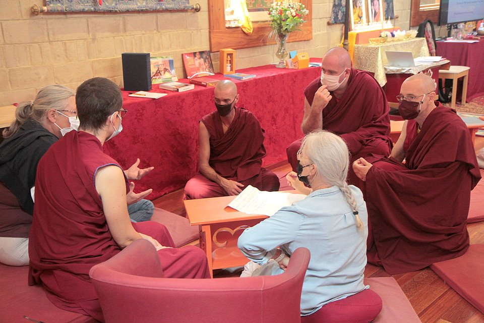 monks and lay students, all wearing masks, sit in a group and talk