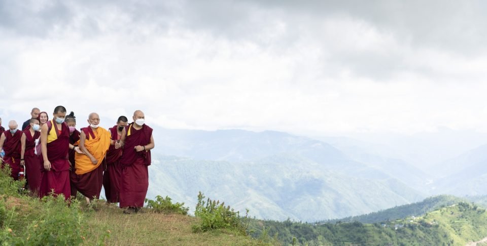 Lama Zopa Rinpoche and monks on a mountain with a vast view