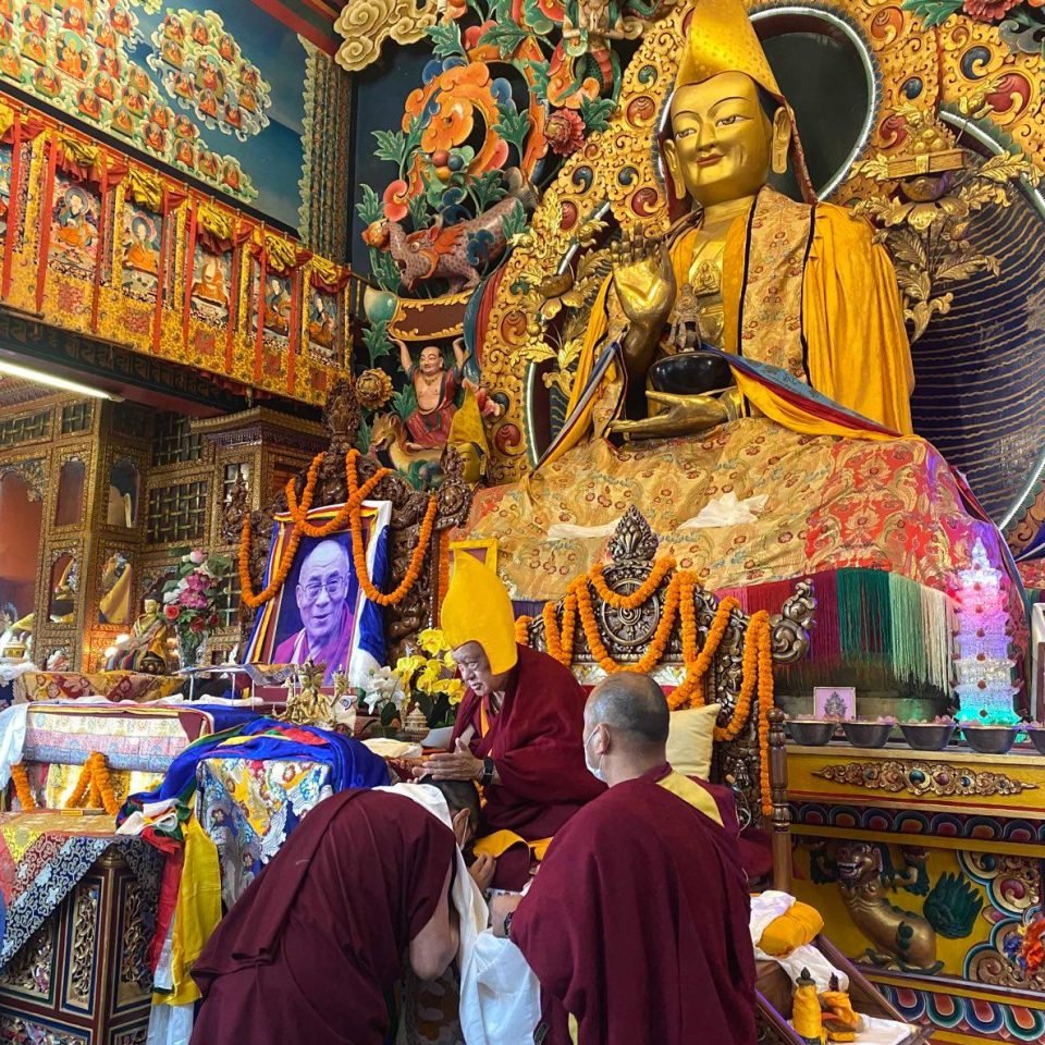 Lama Zopa Rinpoche seated on throne decorated with garlands with monks making offerings