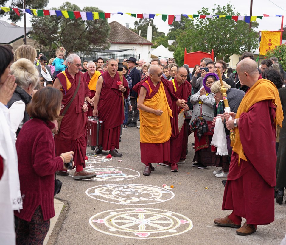 Lama Zopa Rinpoche walking among a crowd of people welcoming him and offering him khatas