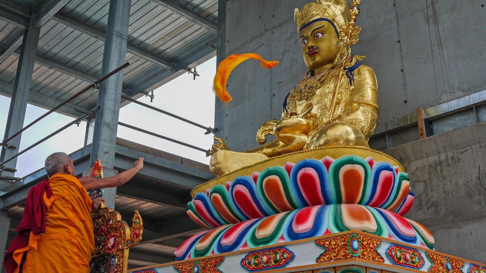 a yellow khata is offered to a large golden statue of Guru Rinpoche 