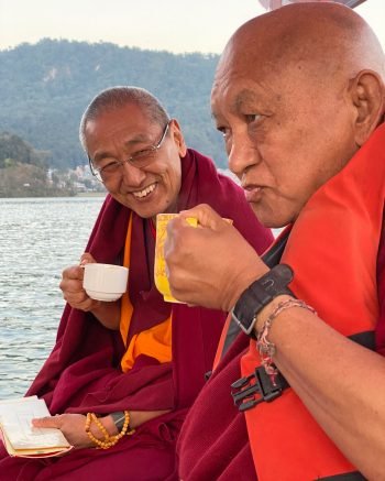 Khen Rinpoche Geshe Chonyi and Lama Zopa Rinpoche holding tea cups while on a boat on a lake