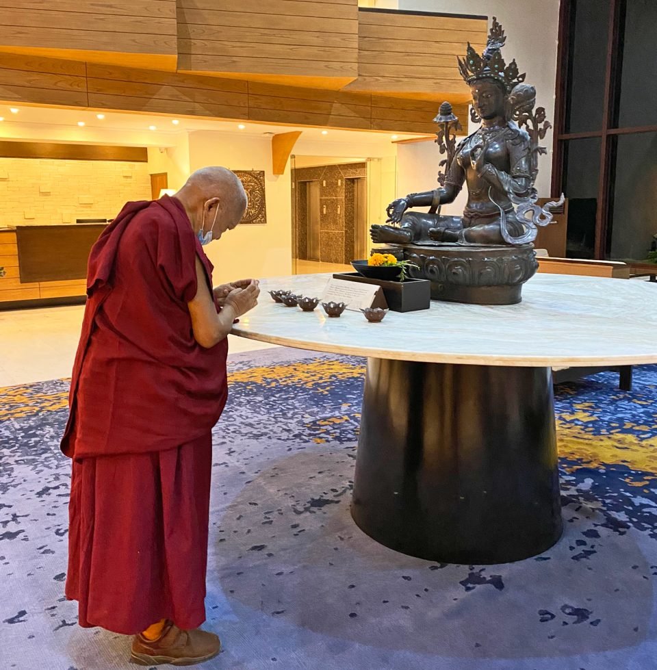 Rinpoche with hands folded and head bowed in front of a Tara statue