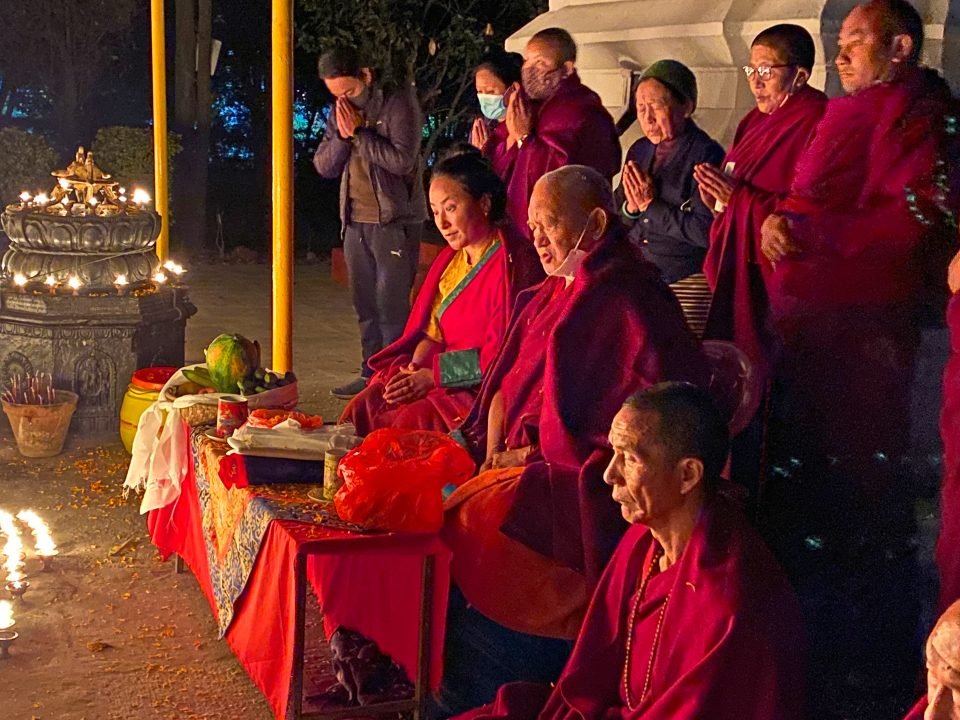 Rinpoche and Khadro-la sitting at puja tables and doing prayers in front of stupa