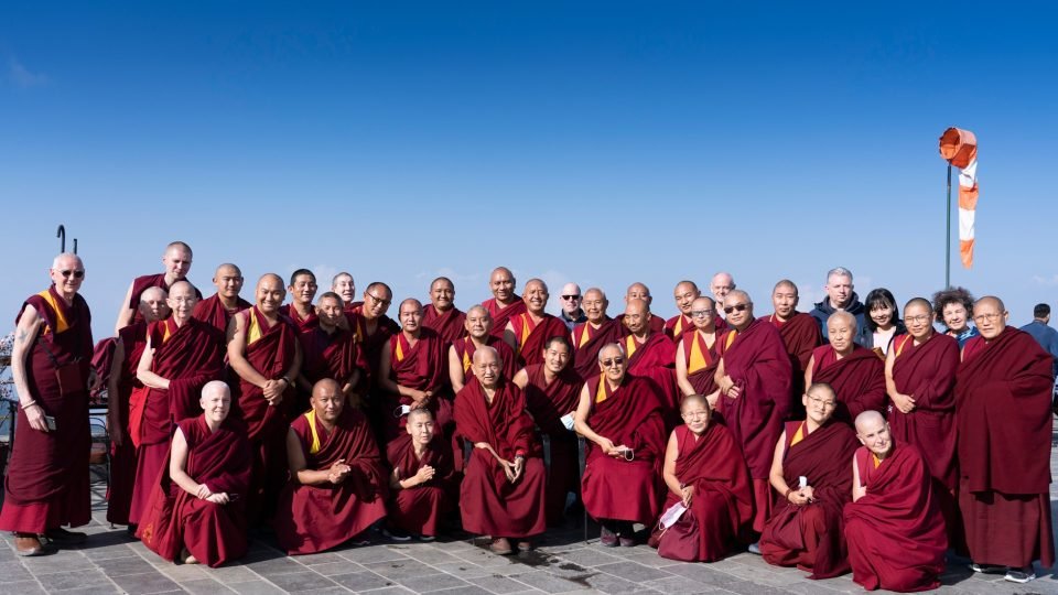 group photo of ordained sangha in maroon robes against a blue sky