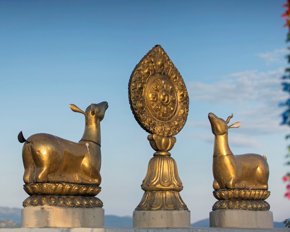 Golden dharmachakra and deer statues with Himalayan foothills in background