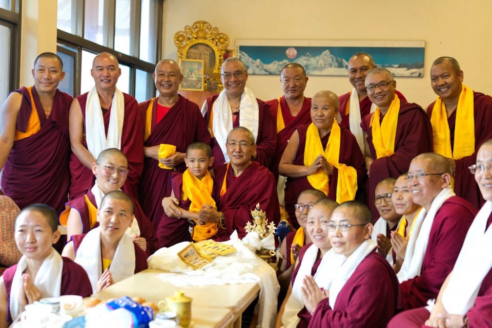 Khen Rinpoche Geshe Thubten Chonyi surrounded by monks and nuns from Kopan Nunnery and Monastery all smiling while wearing khatas and posing for a photo.