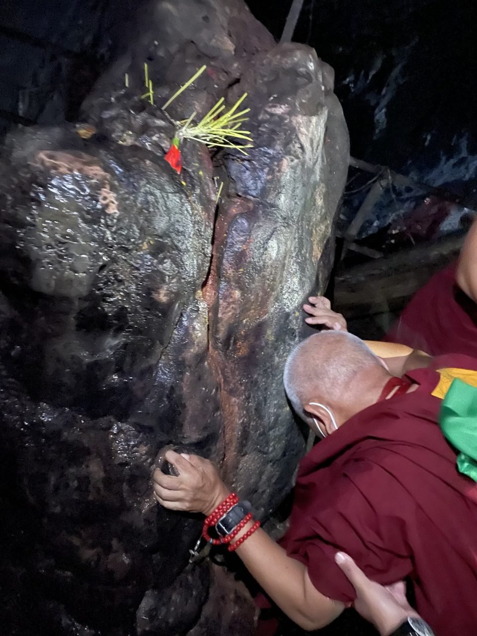 Lama Zopa Rinpoche bending over to touch the crown of his head to a sacred rock formation
