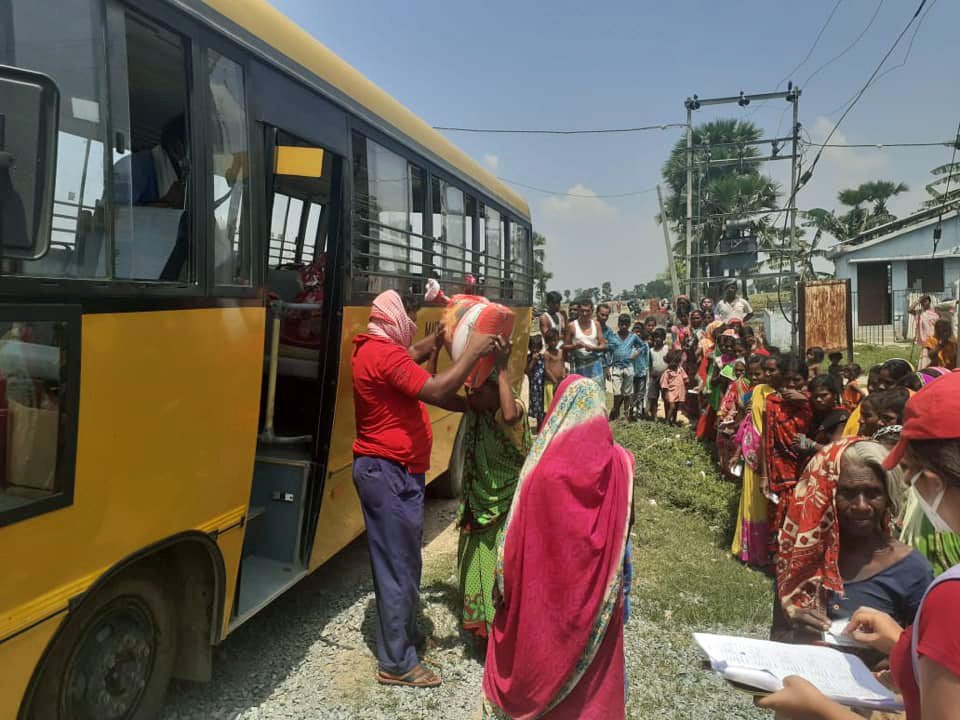 A line of villagers standing alongside the maitreya school bus while Root staff members distribute bags of food to one person at a time..
