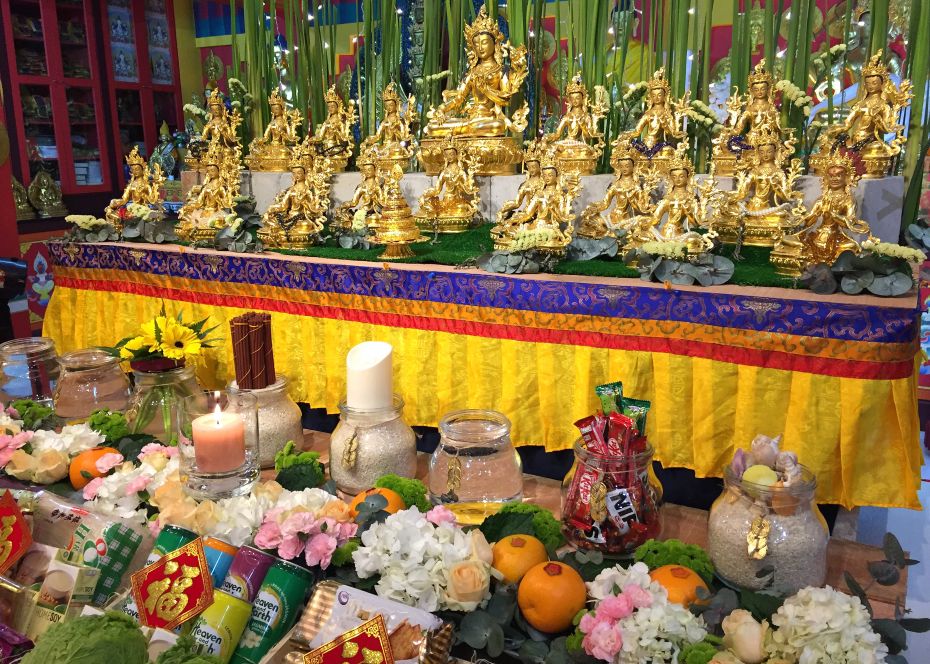 food drink and flower offerings in front of 21 gold colored statues of Tara