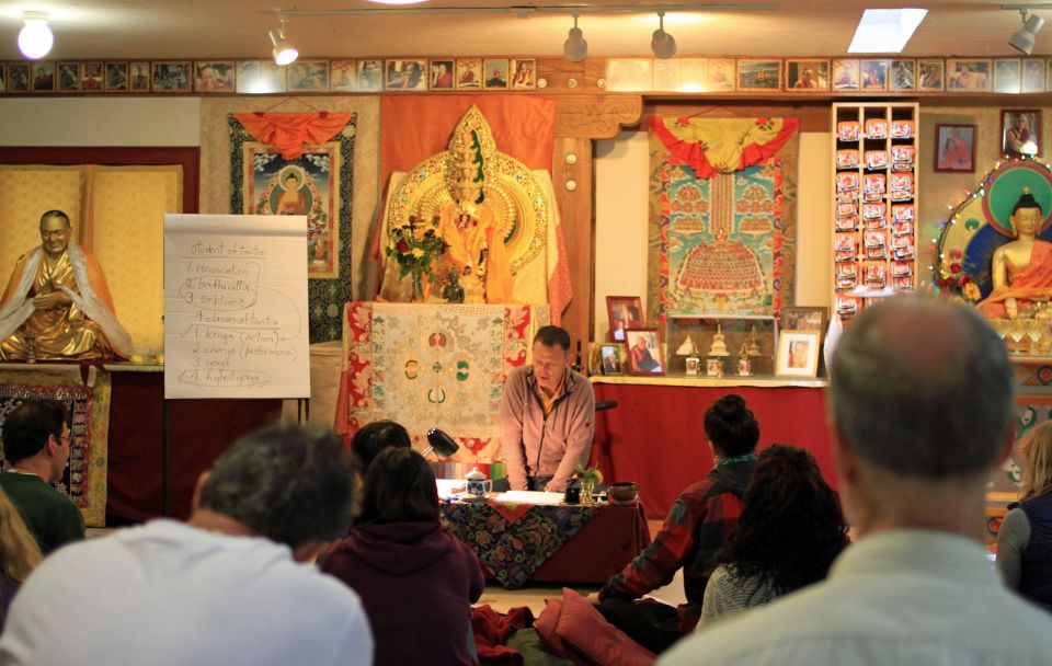 Teacher glen svensson in the front of the gompa behind a low table with an easel next to him with a list of Buddhism principles on the paper and students carefully listening.