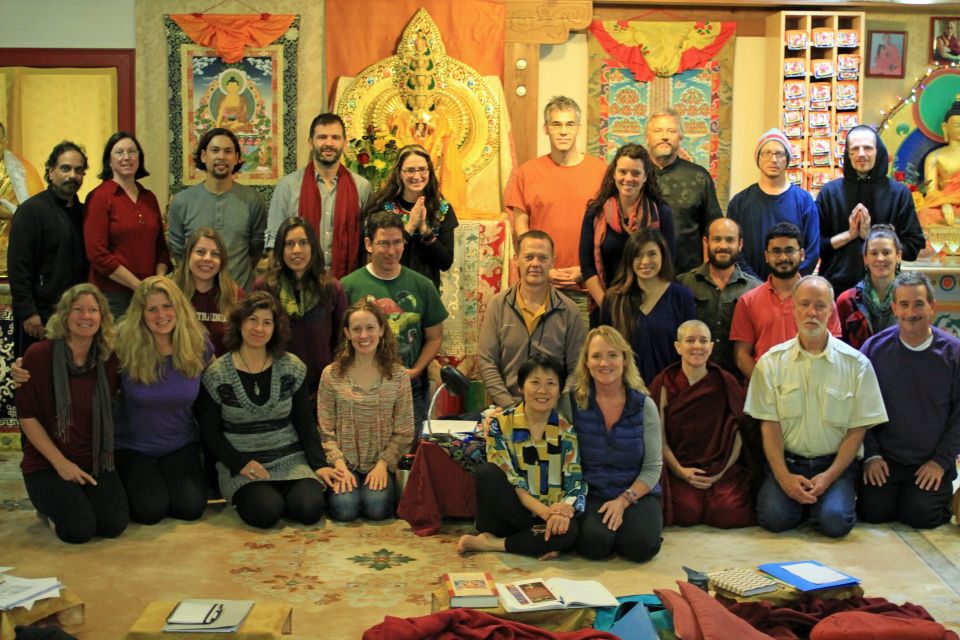 Teacher glen svensson surrounded by a group of students posing for the camera in the vajrapani institute gompa in front of colorful thangkas and statues.
