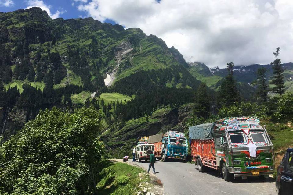 A row of shiny colorfully decorated trucks on the road in a beautiful mountain setting.