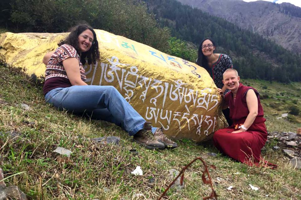 Three Tushita team members seated around a giant gold covered stone covered in white Tibetan writing.