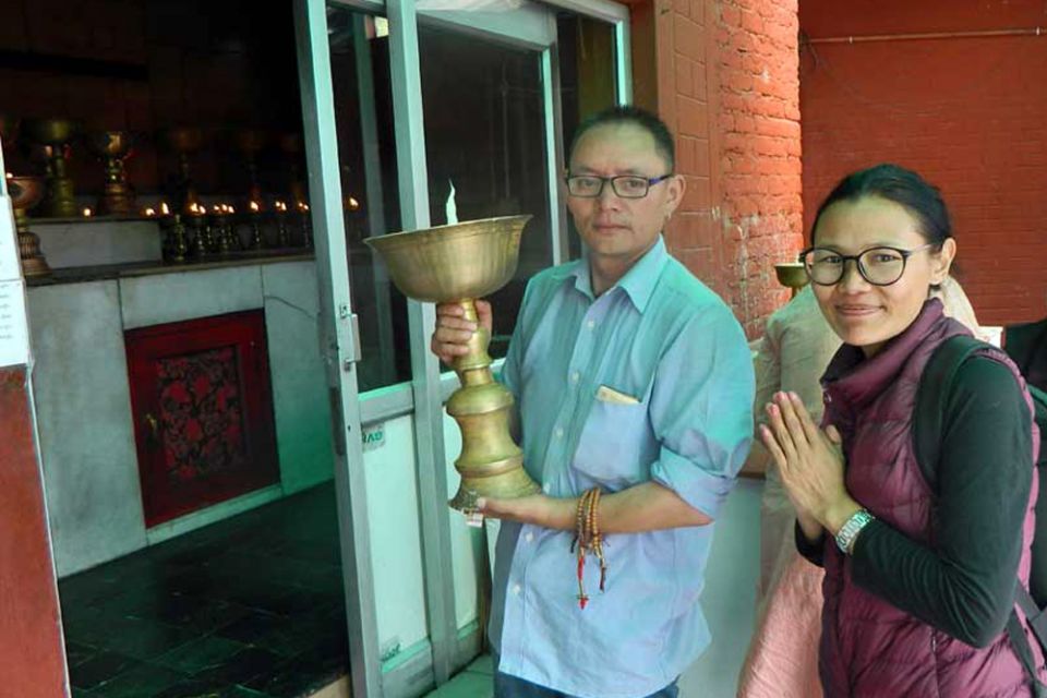 Two Tushita team members offering a very large Tibetan butter lamp in a room with smaller lamps already offered and lit.