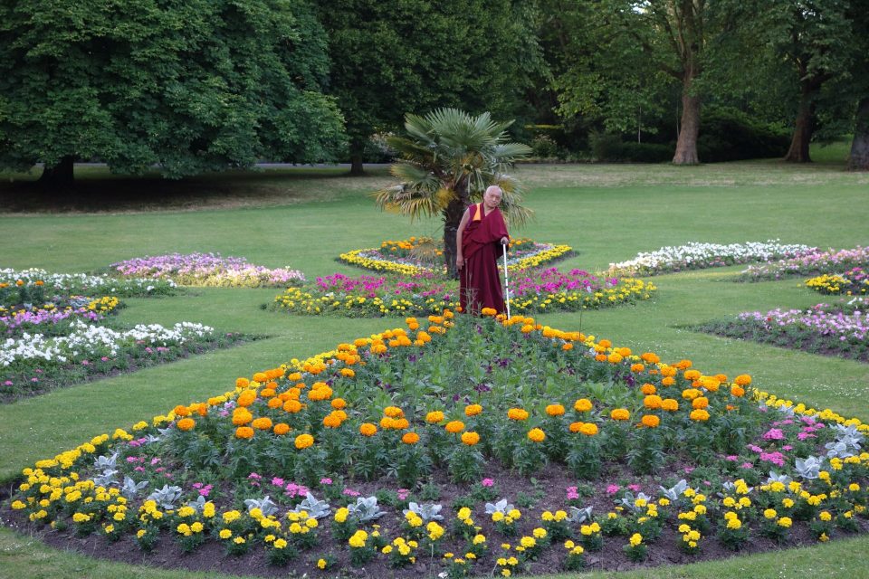 Lama Zopa Rinpoche making flower offerings in a garden in London
